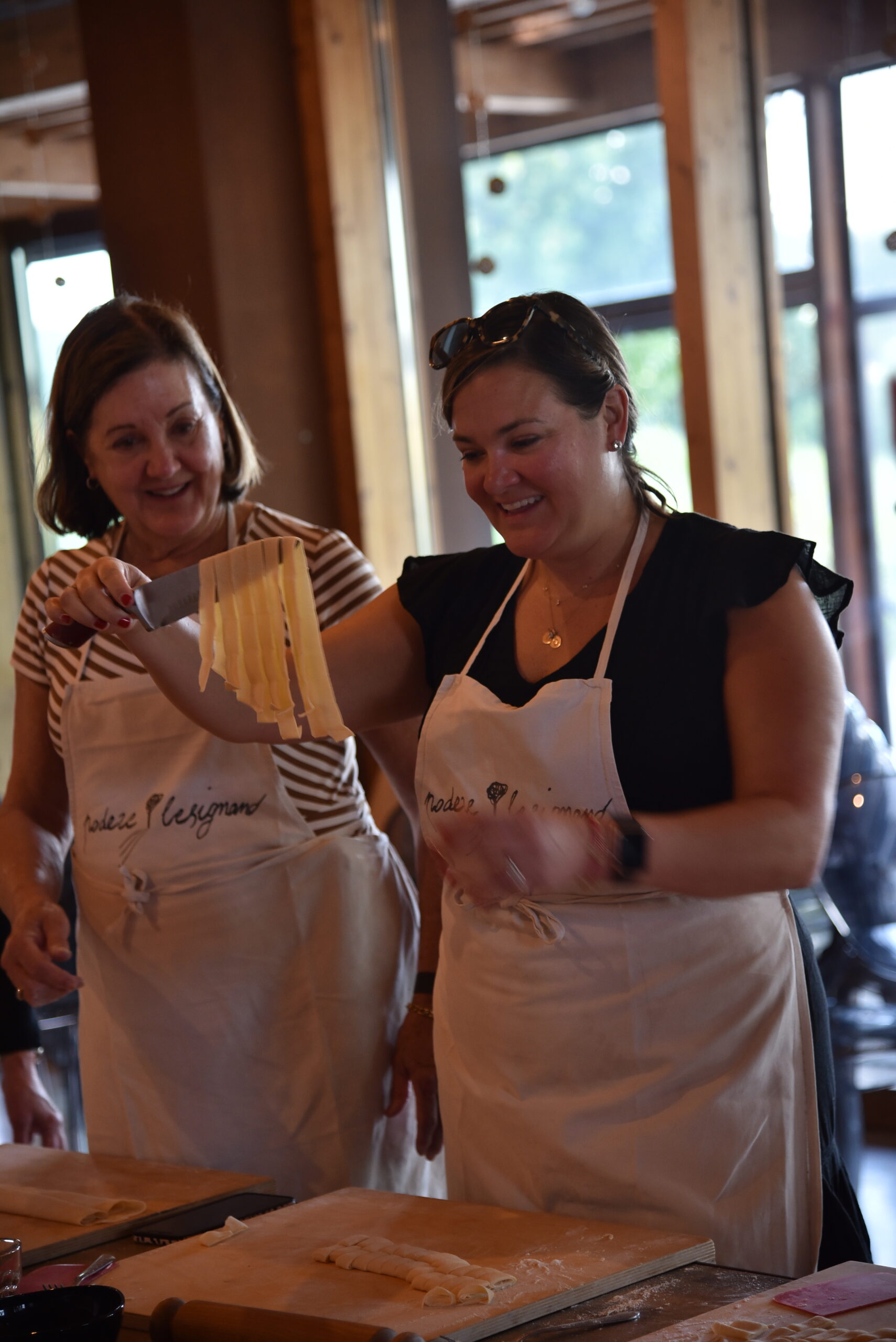 Due donne che ridono si godono il risultato delle loro tagliettele al cooking class. Sorridono e sembrano impressionate dal risultato.